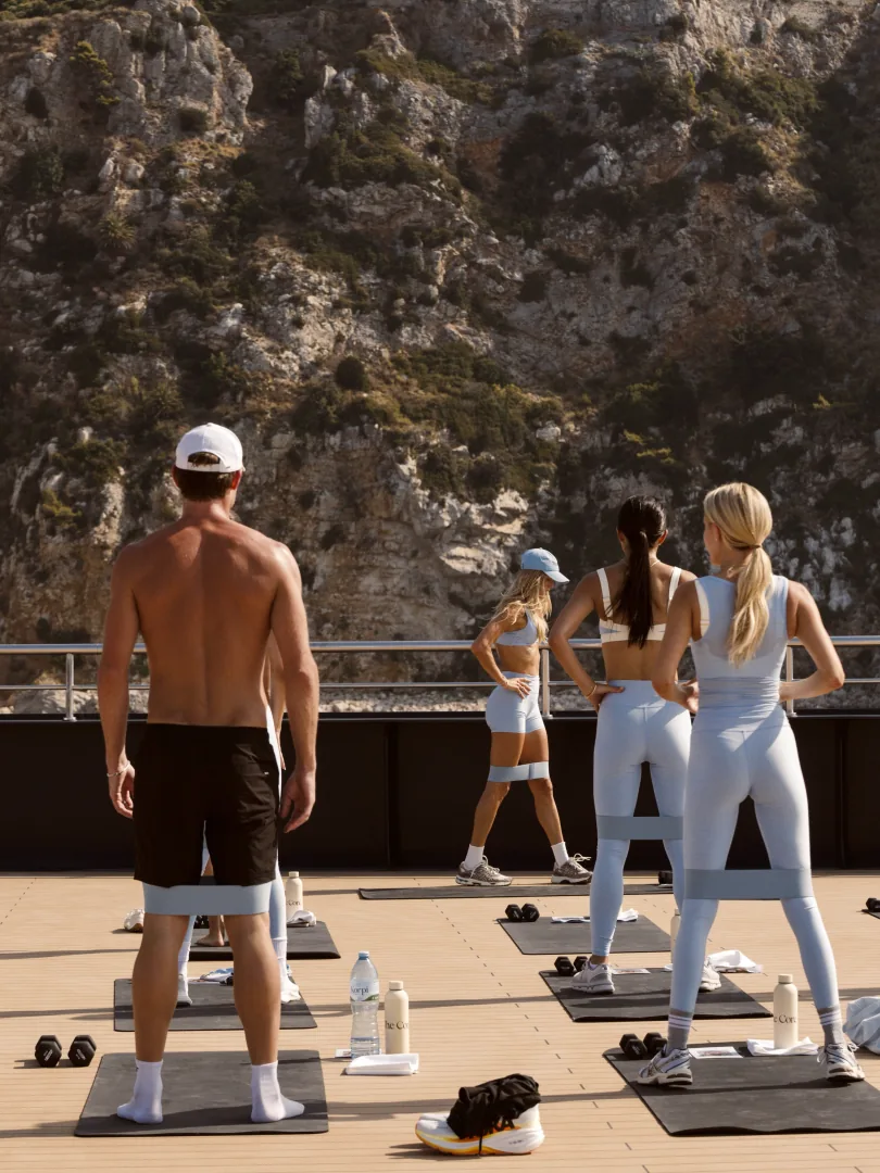 Outdoor group class on a sunlit deck below cliffs, Ritz-Carlton Yacht Collection